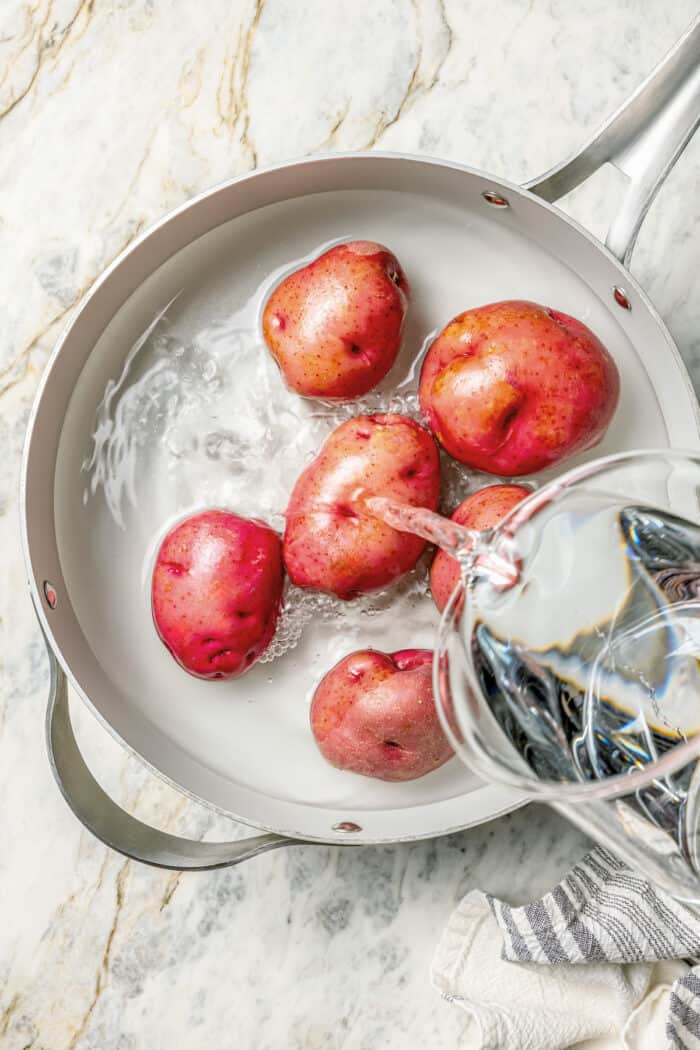 Water is added to red potatoes in a pot.