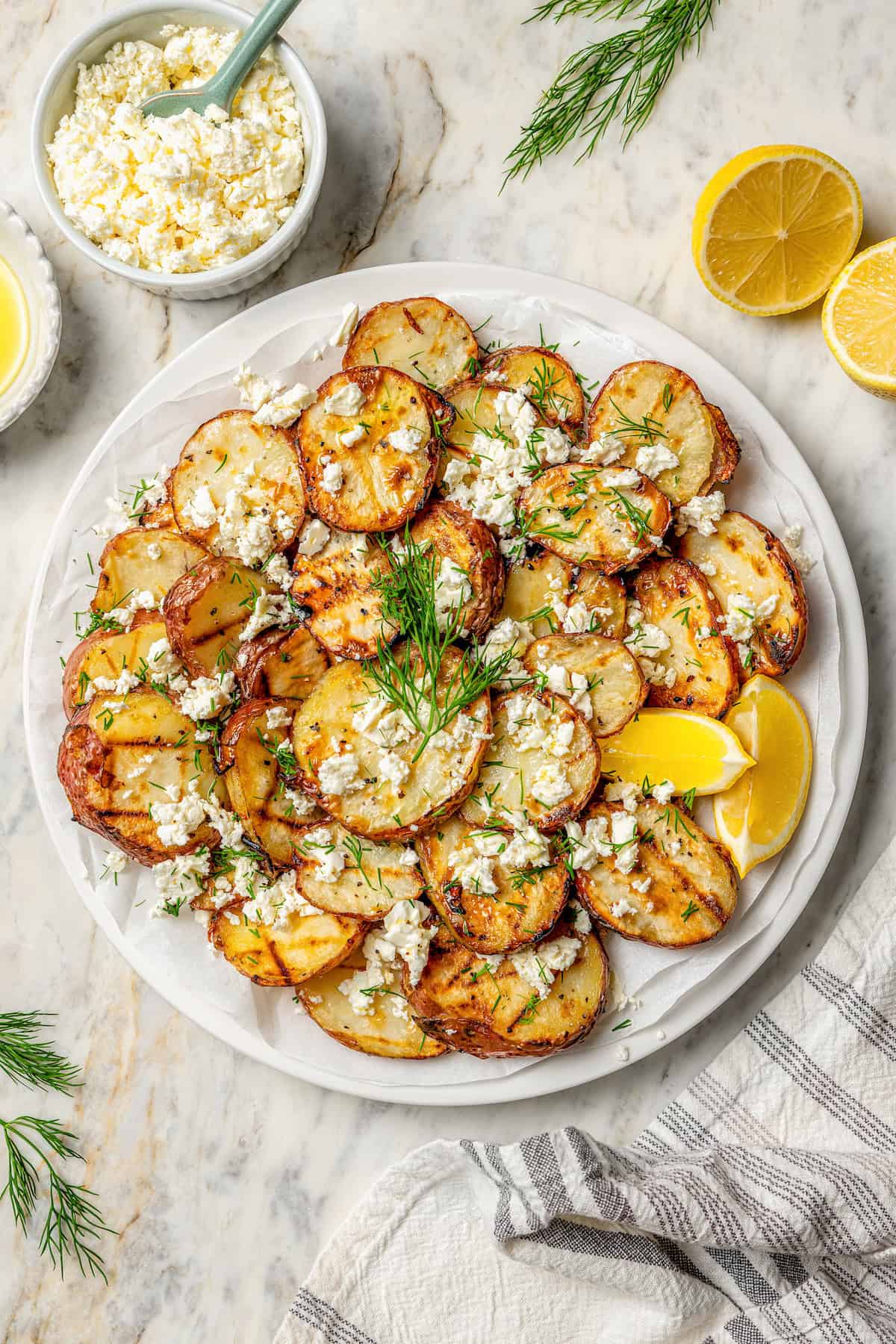 Crisp-tender Grilled Red Potatoes are spiked with the brisk flavors of dill, feta cheese, and lemon and grilled to perfection. A serving platter holds grilled potatoes on a table.