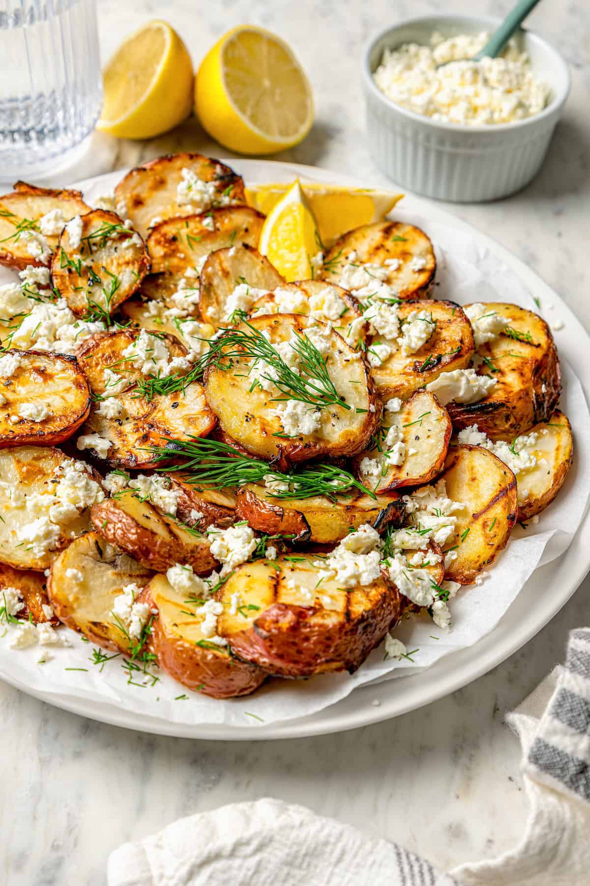 Lemons and a bowl of cheese are in the background with a plate of grilled red potatoes in front of them.