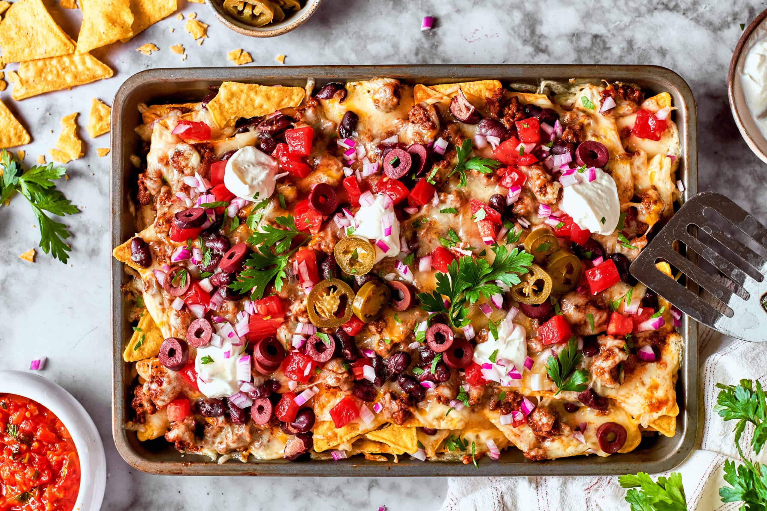 overhead photo of a rimmed pan full of baked cheesy nachos loaded with meat and vegetables