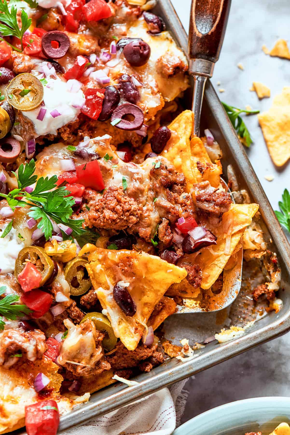 a rimmed pan of macho nachos with a spatula in it
