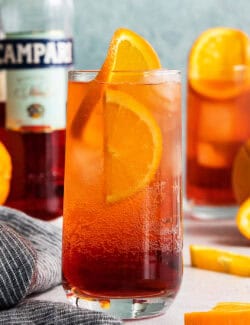A bottle of Campari stands in the background with two Americano cocktails.