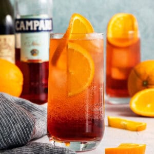 A bottle of Campari stands in the background with two Americano cocktails.