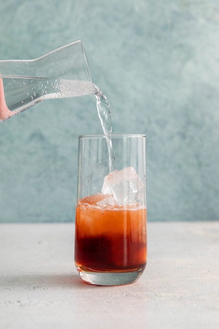 Soda water is added to a glass of Americano cocktail.