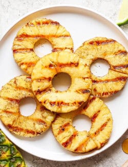 Five rings of grilled pineapple on a white plate.