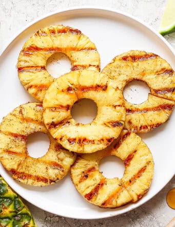 Five rings of grilled pineapple on a white plate.