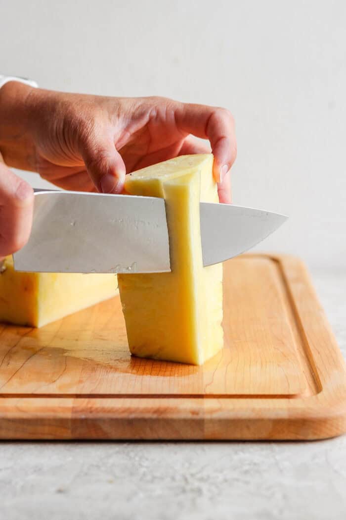 A knife slices through pineapple.
