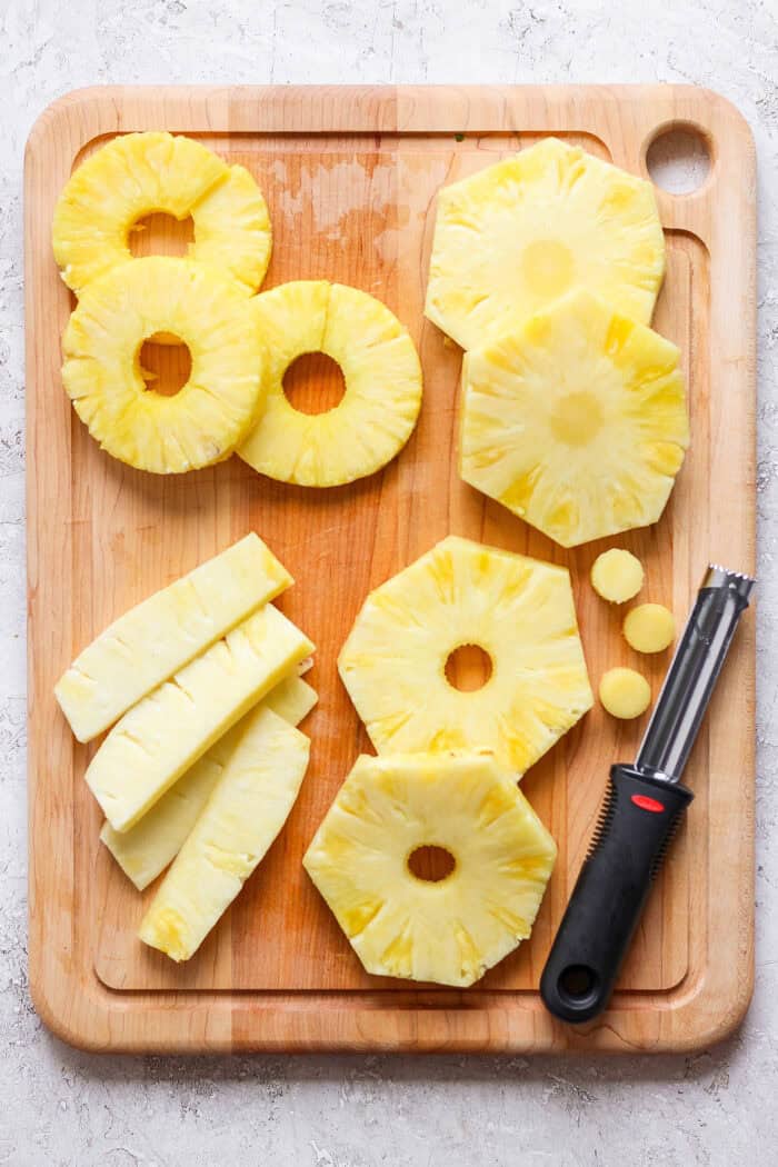 The core is removed from rings of pineapple on a cutting board.