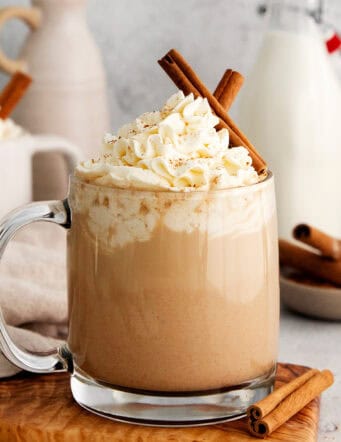 Mugs of pumpkin spice latte are garnished with cinnamon sticks and topped with whipped cream.