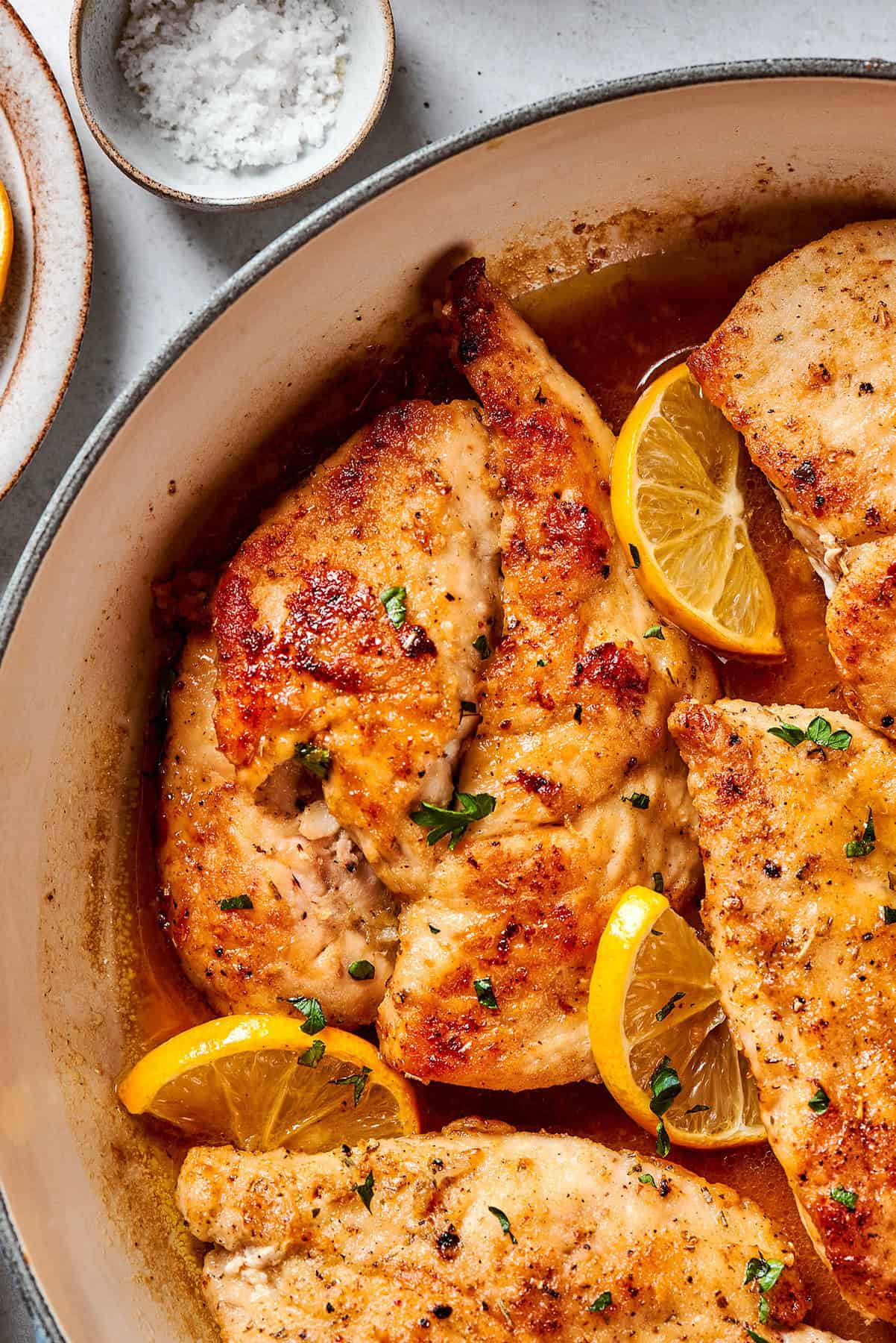 overhead, close photo of chicken breasts in a skillet with lemon and pepper