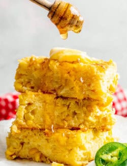 a stack of Jiffy corn casserole pieces, with honey being drizzled over the top