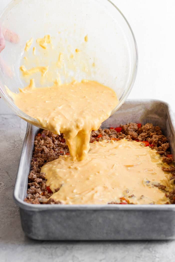 Pouring the egg mixture over the sausage-veggie mixture in the casserole dish. 