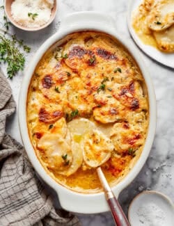 overhead photo of a white oval baking dish with cheesy scalloped potatoes