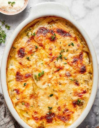 overhead photo of an oval white baking dish of cheesy scalloped potatoes