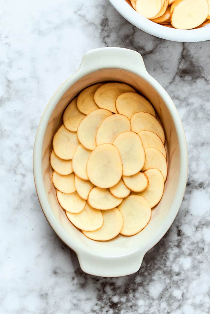 thin potato slices layered in an oval white baking dish
