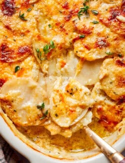 Close-up of cheesy scalloped potatoes with onions, thyme, and rosemary.
