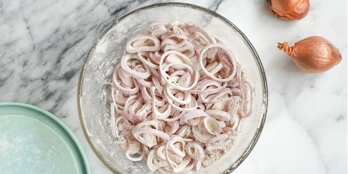 preparing the shallots for frying, coating them with a spiced flour mixture
