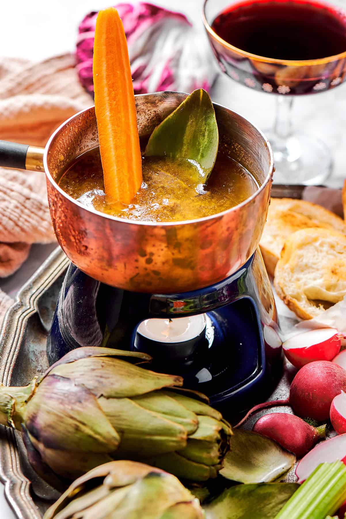 a small pot of bagna cauda with a candle burning underneath, plus fresh vegetables for dipping