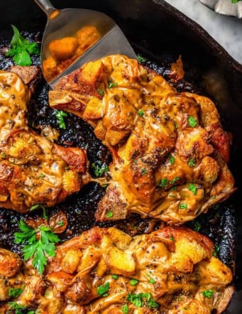a cast iron skillet with juicy baked pork chops covered in stuffing and gravy
