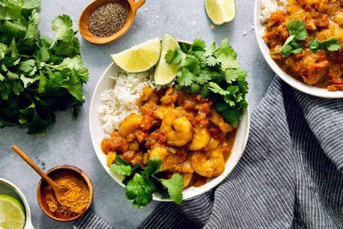 Overhead view of shrimp curry in bowl with rice, cilantro, and lime wedges