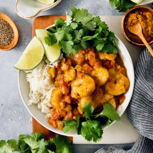 Overhead view of shrimp curry in bowl with rice, cilantro, and lime wedges