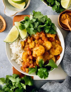 Overhead view of shrimp curry in bowl with rice, cilantro, and lime wedges