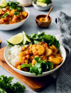 Bowl of shrimp curry with rice, cilantro, and lime wedges