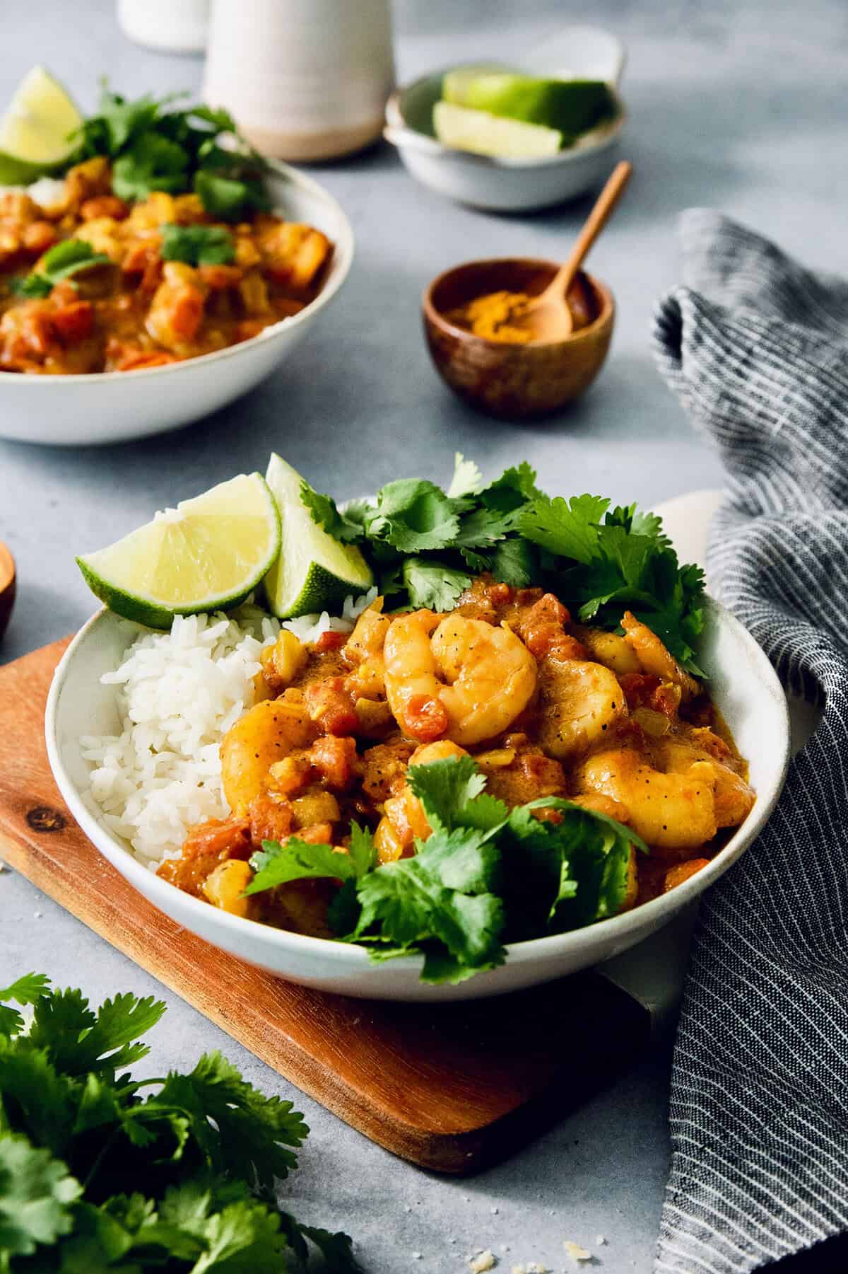 Bowl of shrimp curry with rice, cilantro, and lime wedges