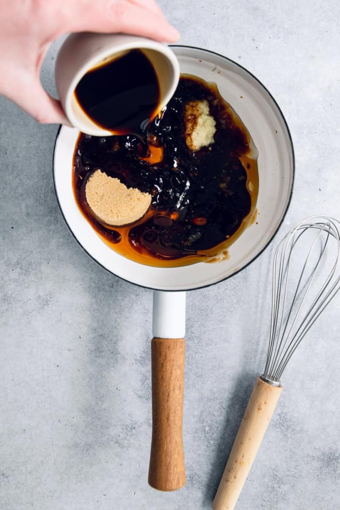 Pouring soy sauce into pan of ingredients for teriyaki sauce