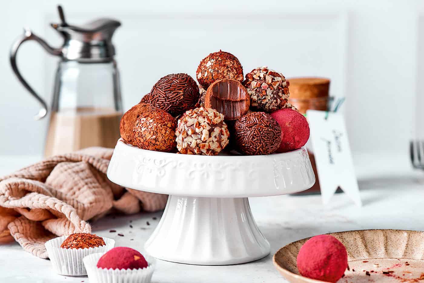 chocolate truffles rolled in a variety of coatings, on a white pedestal platter