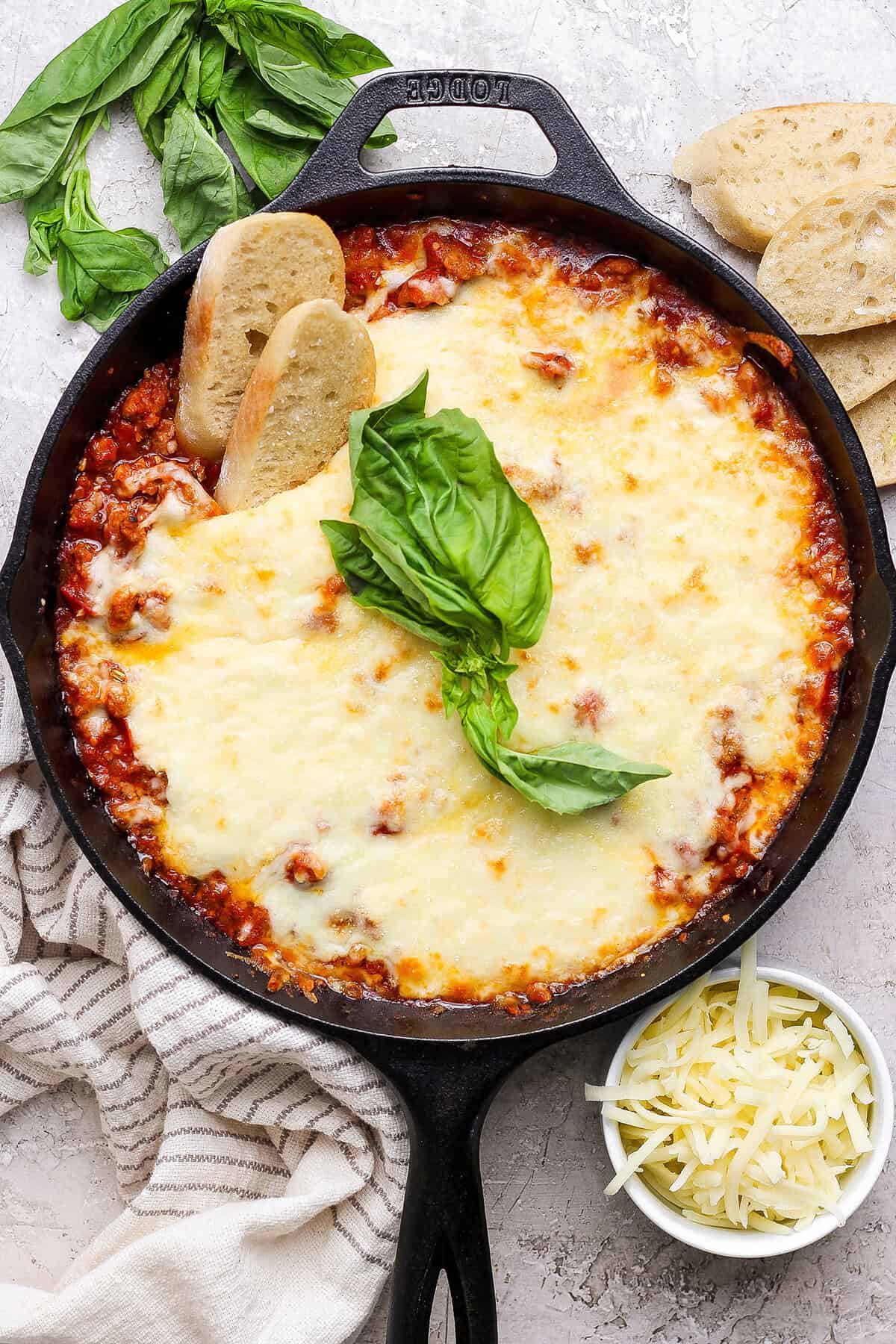 This Lasagna Dip has melty pockets of cheese, meaty sausage, and zesty tomato sauce, all ready for scooping with garlic bread dippers. YUM! Overhead view of lasagna dip in skillet with two sliced baguette dippers