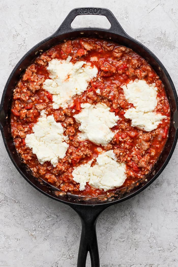 Dollops of cheesy yum added to meaty sauce in skillet