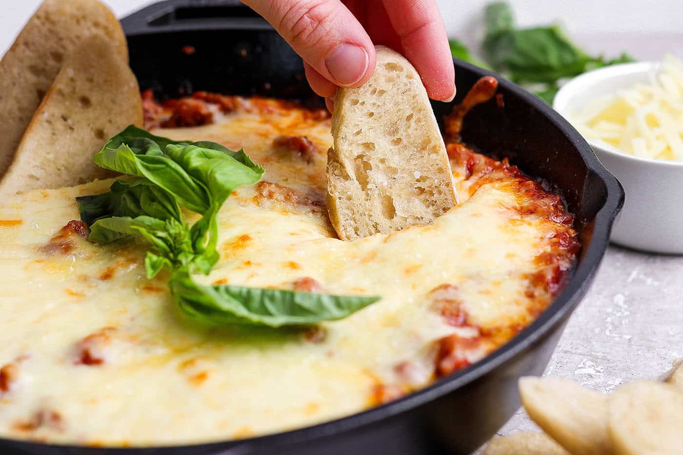Baguette dipper in skillet of lasagna dip