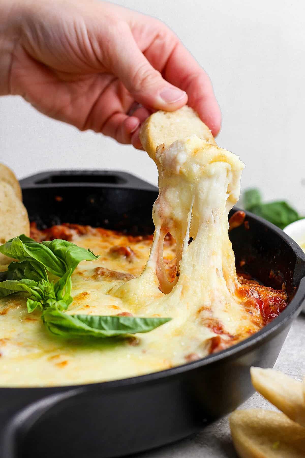 Dipping baguette into cheesy lasagna dip