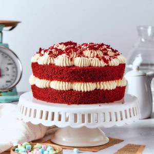 a double layer red velvet cake with cream cheese frosting on a white pedestal