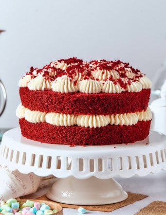 a double layer red velvet cake with cream cheese frosting on a white pedestal