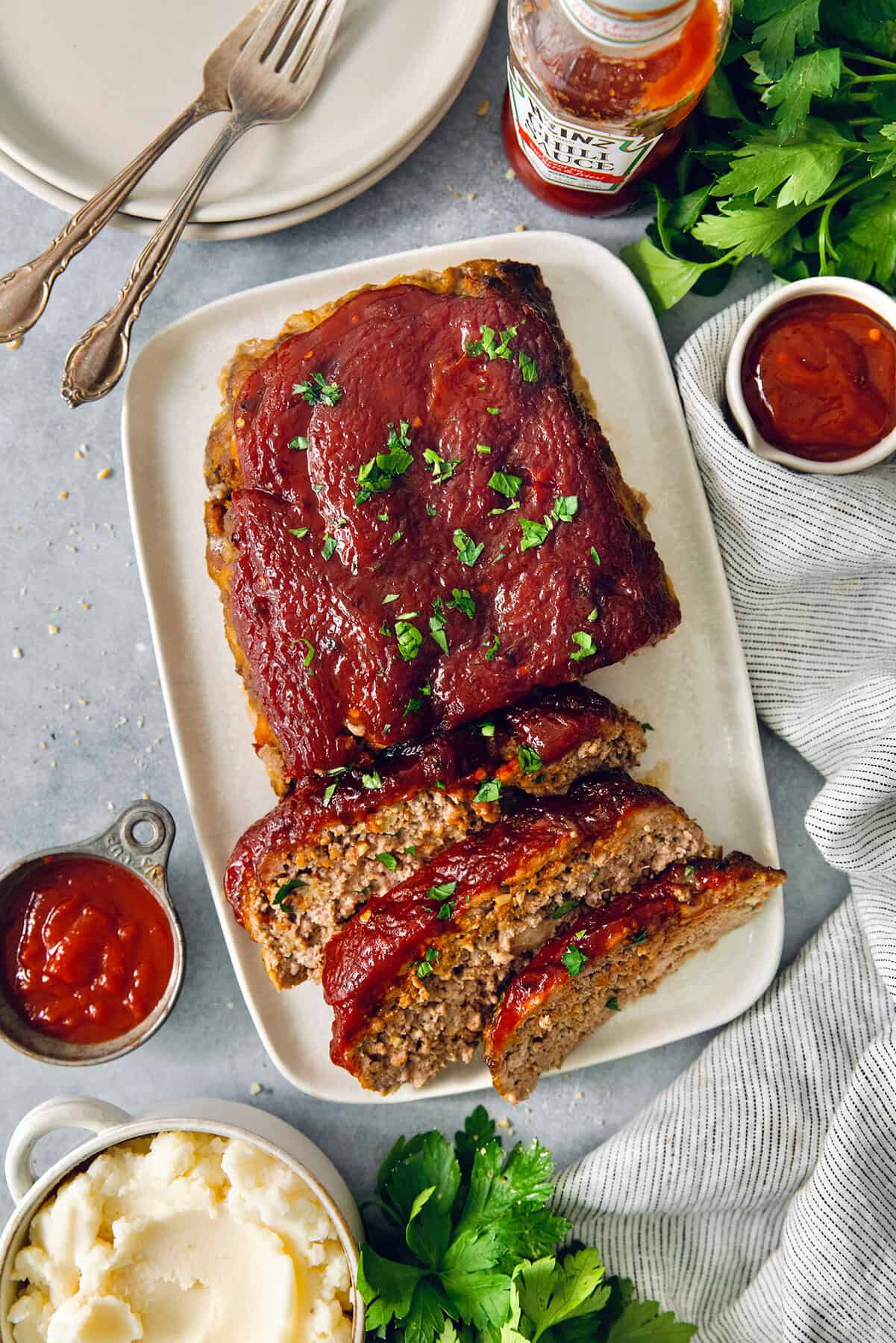 This Air Fryer Meatloaf gives you a classic comfort food meal — without the hassle of an oven. Tender and juicy, with the perfect glaze! Overhead view of air fryer meatloaf on platter with three slices cut