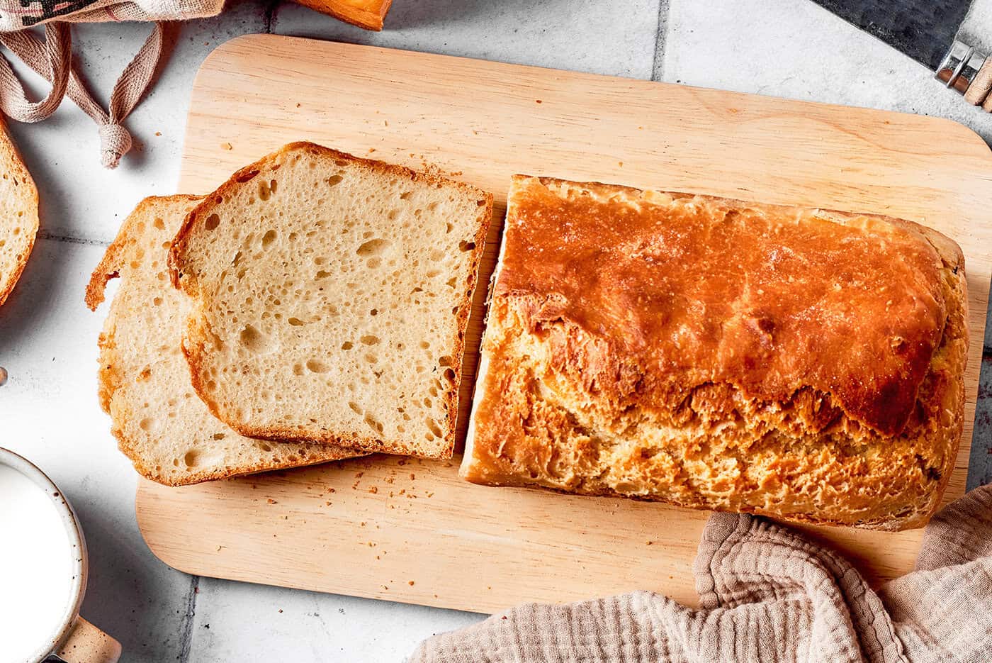 Overhead photo of English muffin bread loaf on a wood board, with slices cut from the loaf