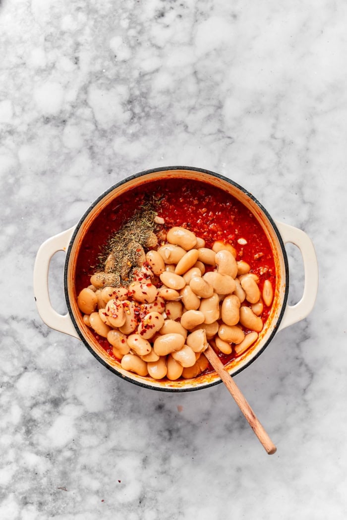 Gigante beans added to pot of tomato sauce with seasonings