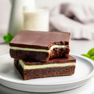 two layered chocolate mint brownies on a plate, one with a bite out of it