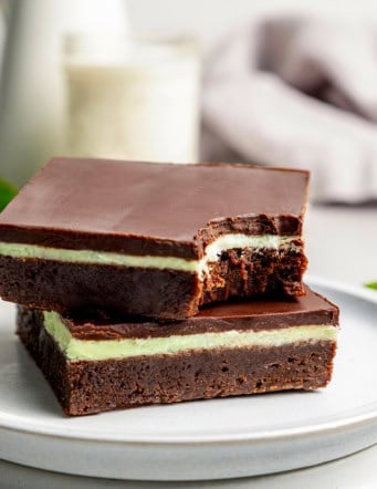 two layered chocolate mint brownies on a plate, one with a bite out of it