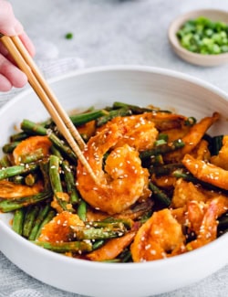Chopsticks picking up Hunan shrimp from bowl
