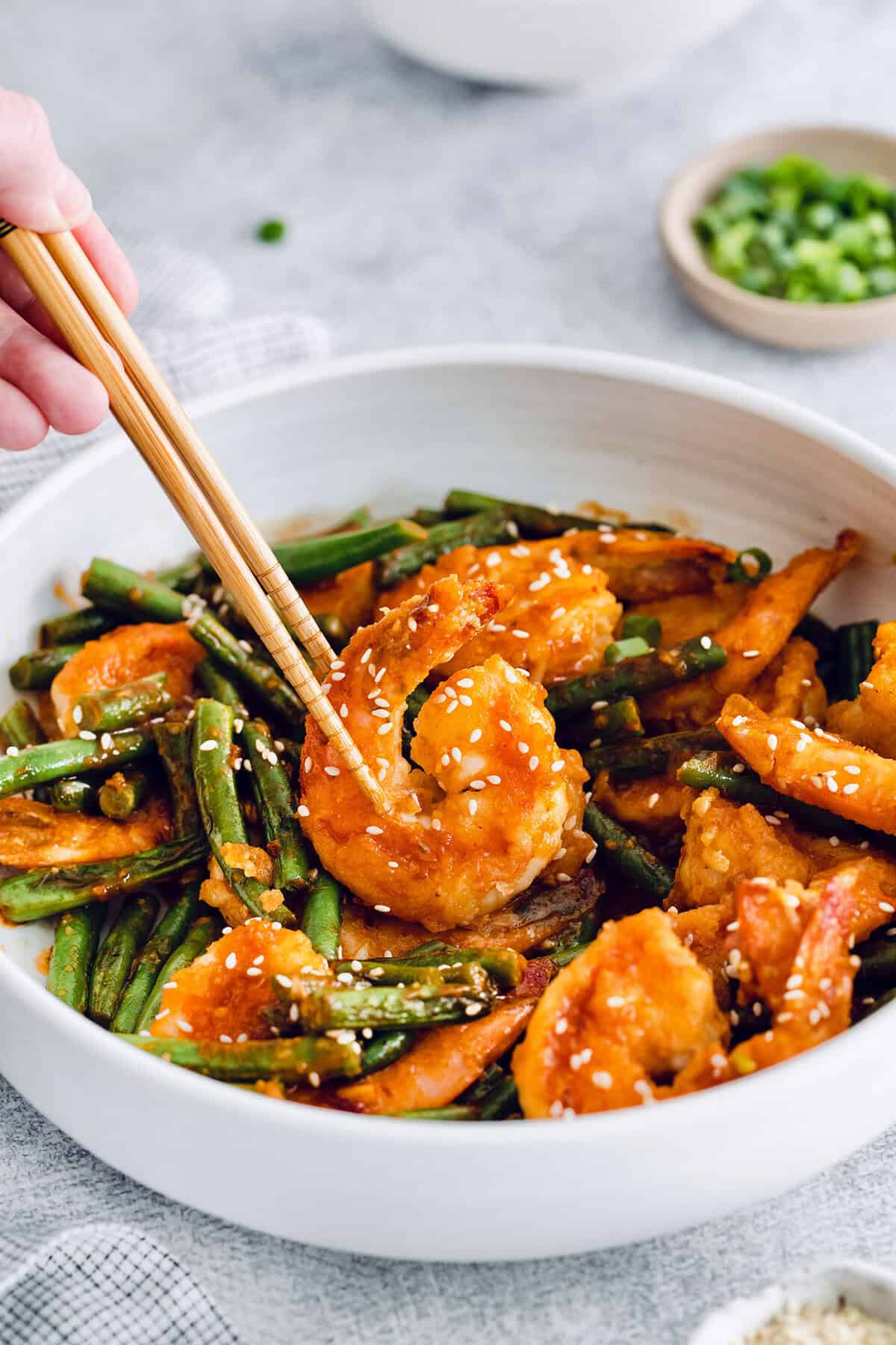 These Hunan shrimp are crisp and juicy, with a spicy, smoky chili sauce and fresh blistered green beans. Done in just 20 minutes! Chopsticks picking up Hunan shrimp from bowl