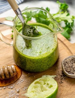 Spoon in small glass pitcher of cilantro lime vinaigrette