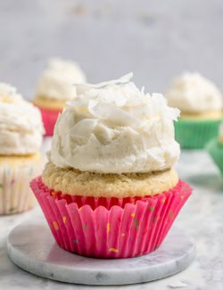 A coconut cupcake with a mound of fluffy coconut frosting, in a pink cupcake liner