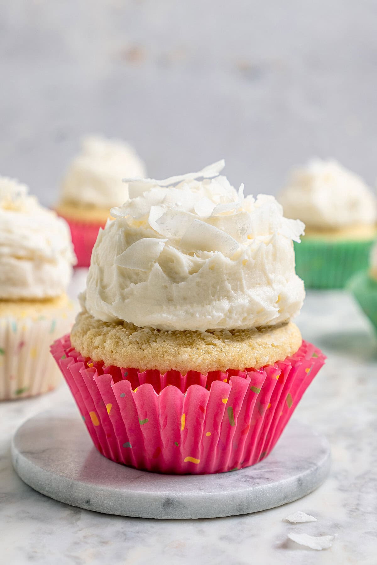 These coconut cupcakes are moist and full of coconut flavor — and just wait until you sink your teeth into the coconut buttercream frosting! A coconut cupcake with a mound of fluffy coconut frosting, in a pink cupcake liner