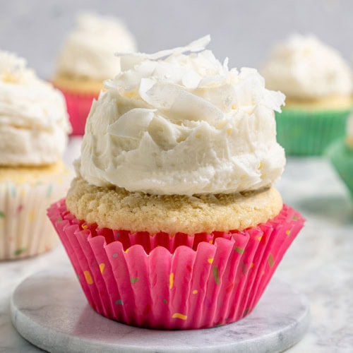 A coconut cupcake with a mound of fluffy coconut frosting, in a pink cupcake liner