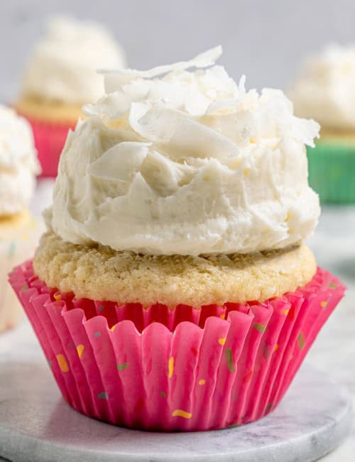 A coconut cupcake with a mound of fluffy coconut frosting, in a pink cupcake liner