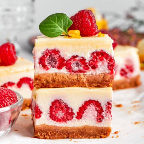 two lemon cheesecake bars with fresh raspberries, stacked on top of each other