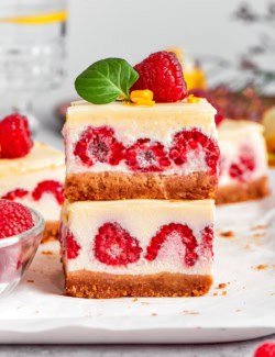 two lemon cheesecake bars with fresh raspberries, stacked on top of each other